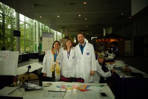 Sonia Singhal, Carrie Glenney, and Brian Connelly in front of the activity table at the Pacific Science Center's UW-centric "Paws-On-Science" event.